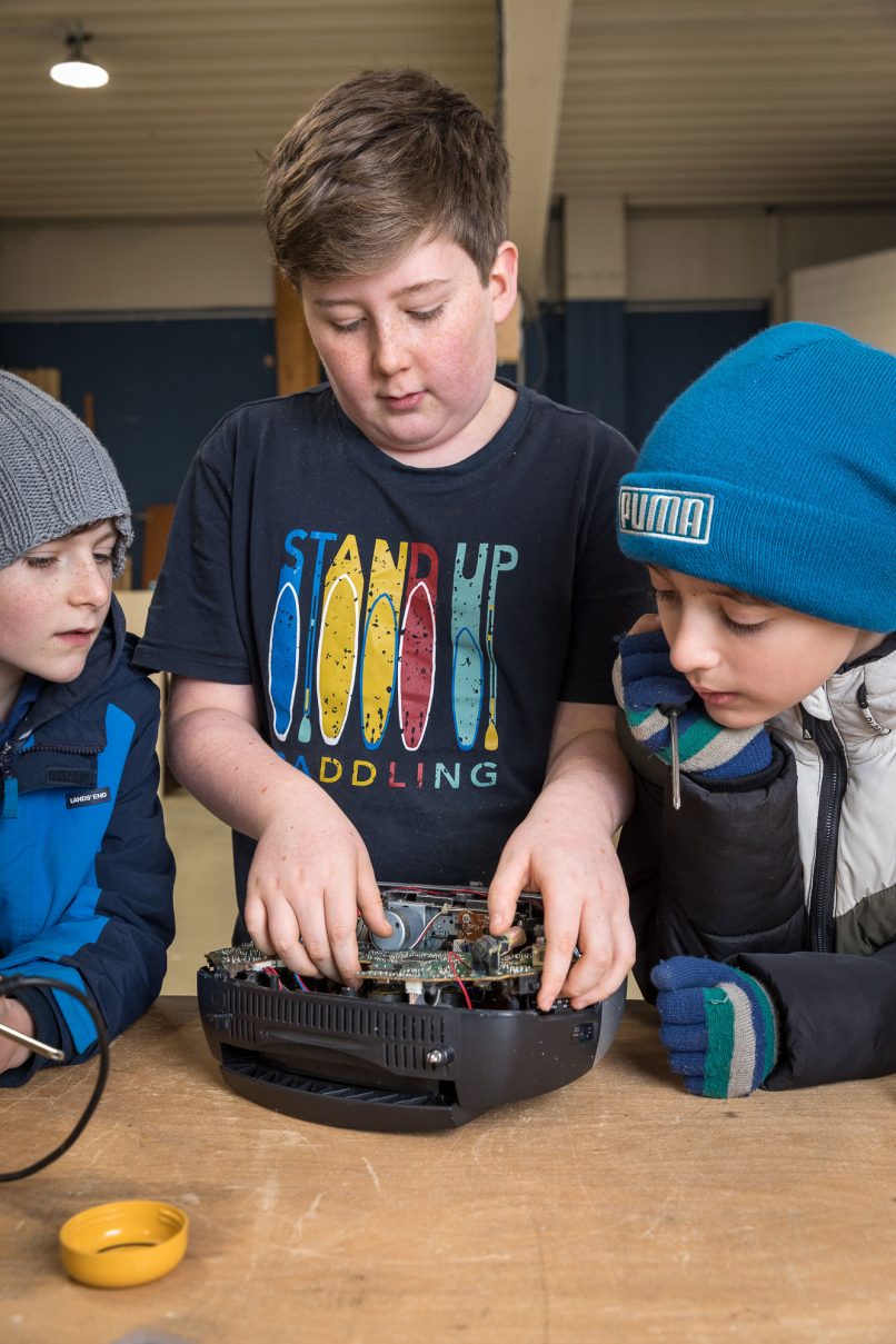 Drei Jungs schauen auf ein kaputtes Elektrogerät