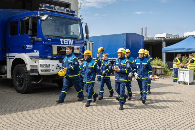 Eine Gruppe Jugendlicher THW-Freiwilliger läuft vor einem Einsatzfahrzeug des THW. Sie sind auf dem Weg, um ihr Leistungsabzeichen abzulegen.