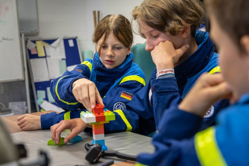 Caja mit anderen Kindern bei einer Funkübung. Gemeinsam müssen sie eine Geschicklichkeitsaufgabe lösen, die sie per Funk gestellt bekommen.